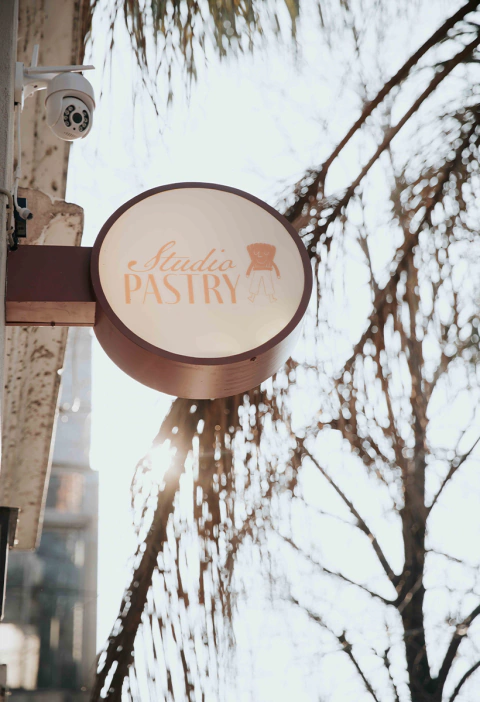 Cartel colgante del Studio Pastry con luz filtrándose entre las ramas